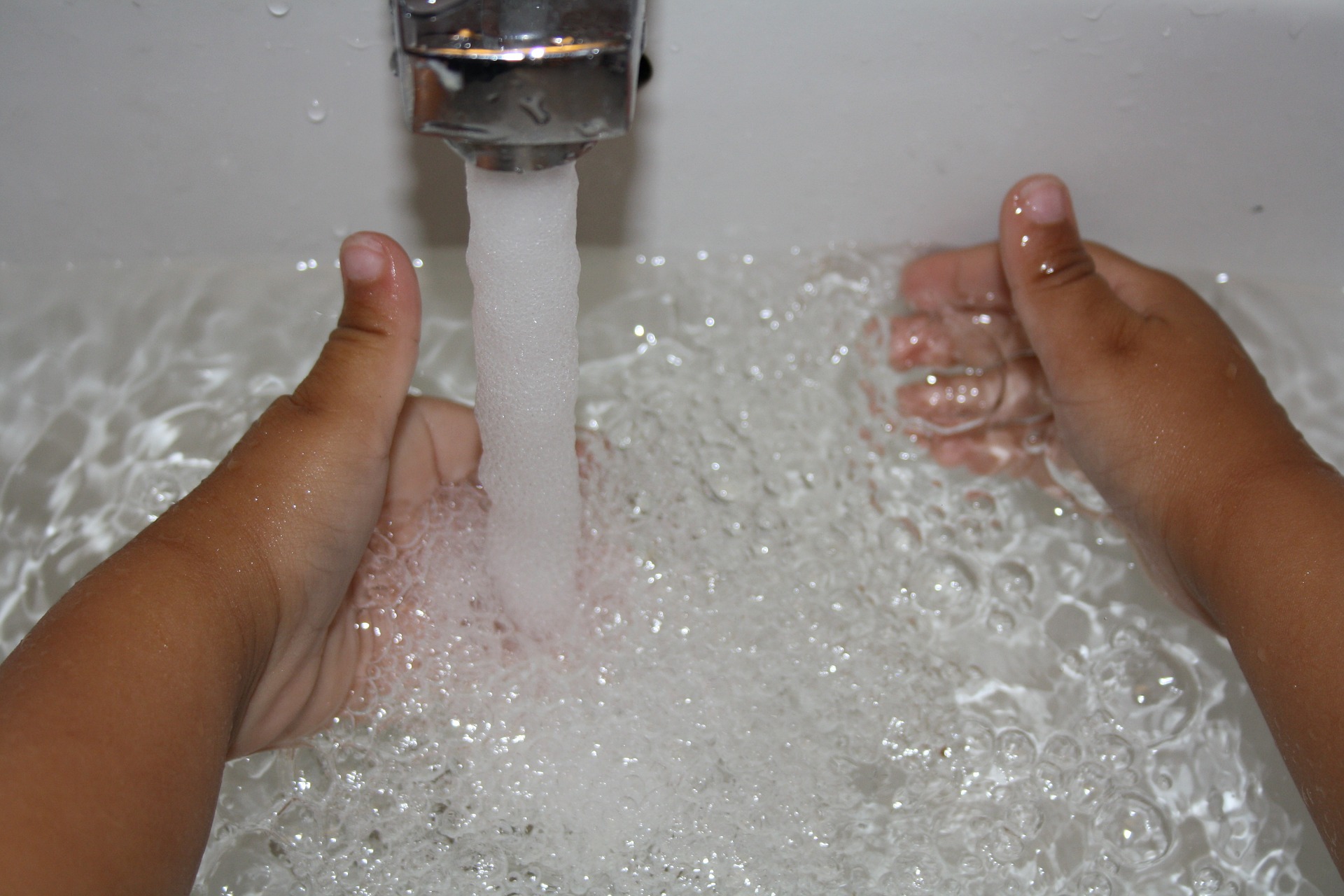 Vatten som rinner ur en vattenkran med två barnhänder i vattnet